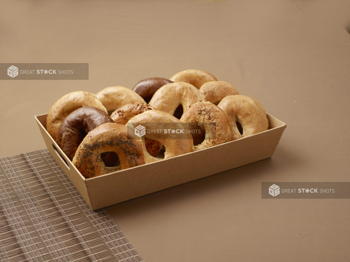 A Wood Tray of Freshly Baked Assorted Bagels for Catering Against a Brown Background - Variation