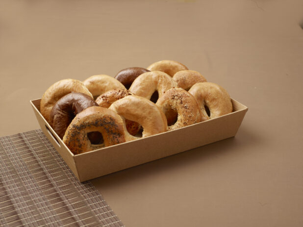 A Wood Tray of Freshly Baked Assorted Bagels for Catering Against a Brown Background - Variation