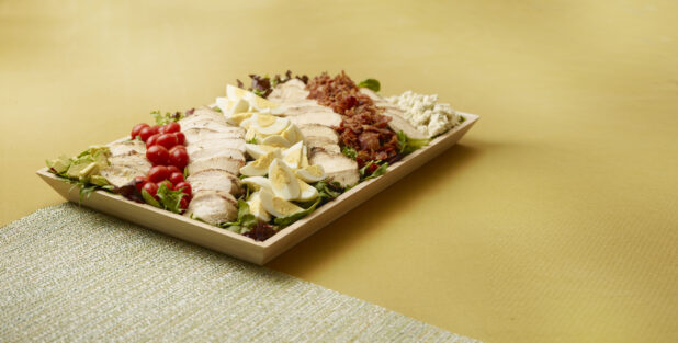 large cobb salad in a wood catering tray on a yellow surface