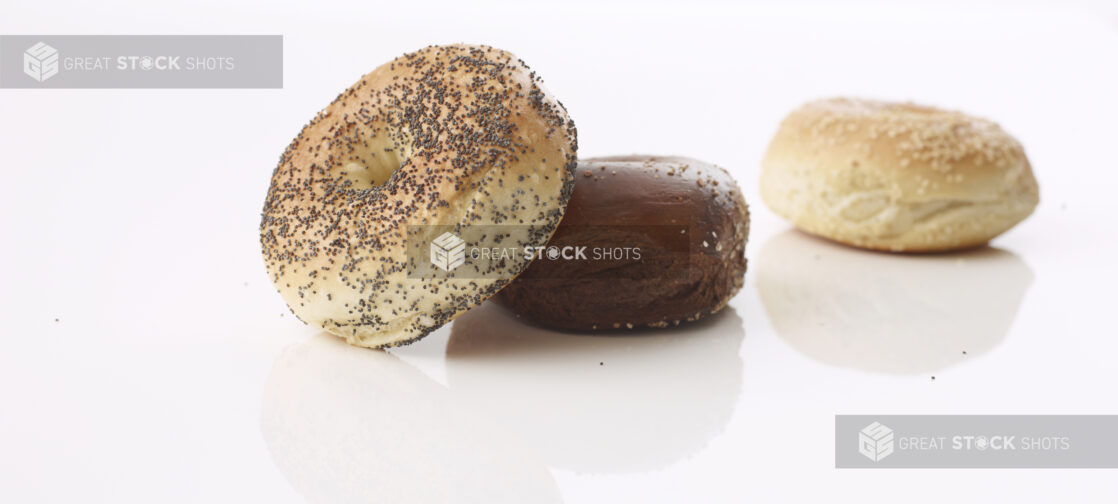 poppy seed bagel resting on a pumpernickel bagel with a sesame seed bagel out of focus in the back ground