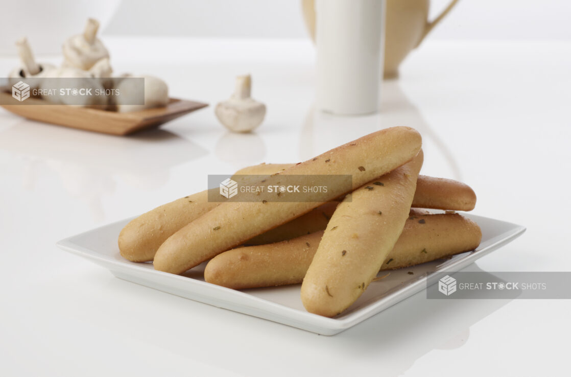 A Pile of Garlic Bread Sticks on a Square White Plate Shot on White