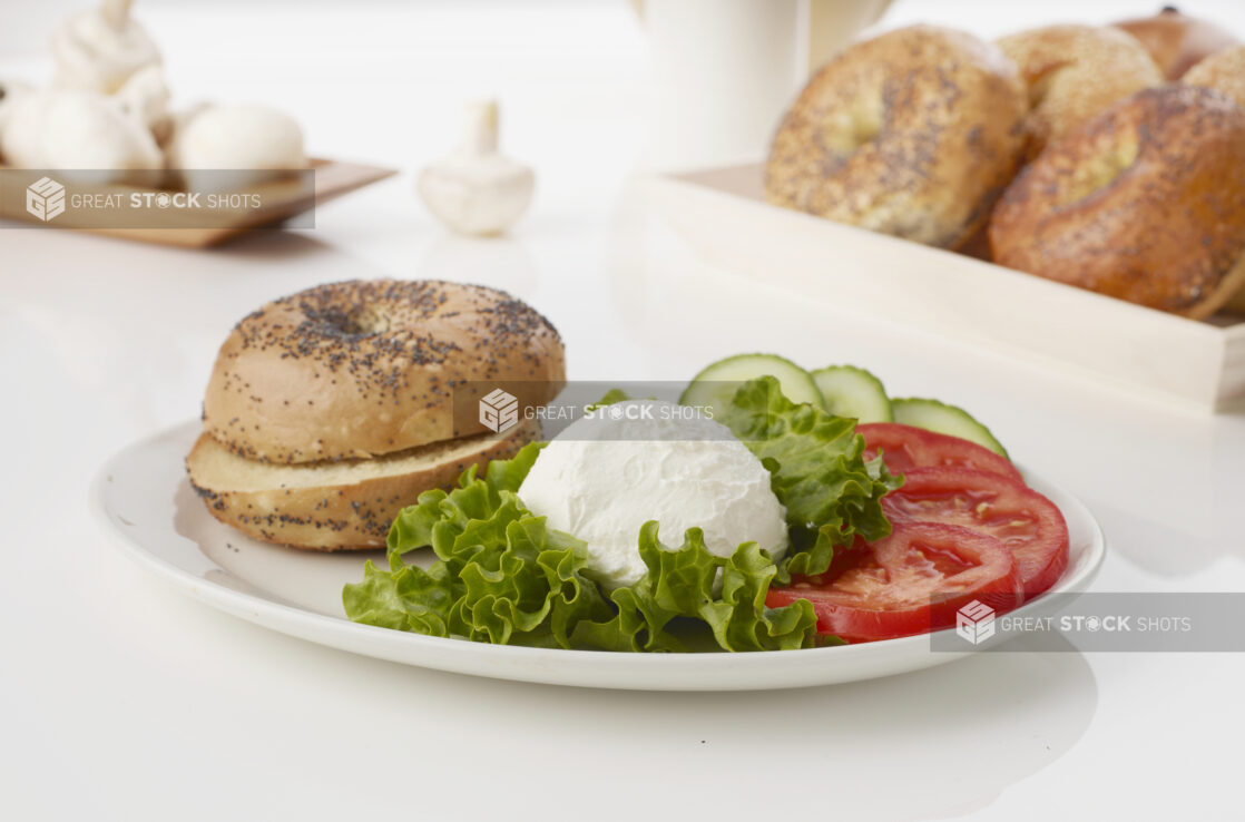 Cream cheese platter with poppy seed bagels fresh tomatoes and cucumber on white background