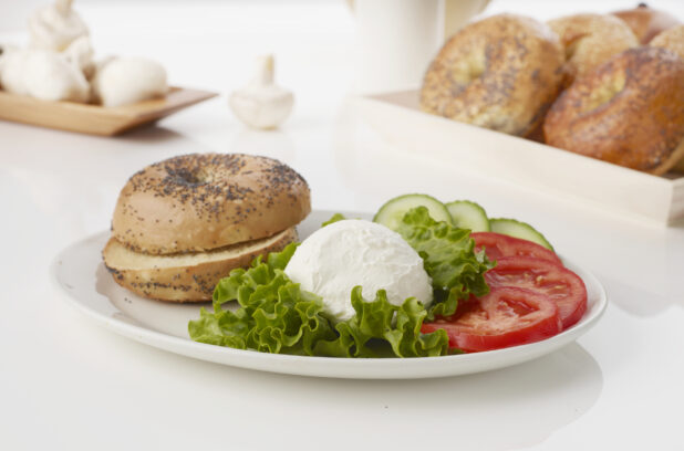 Cream cheese platter with poppy seed bagels fresh tomatoes and cucumber on white background