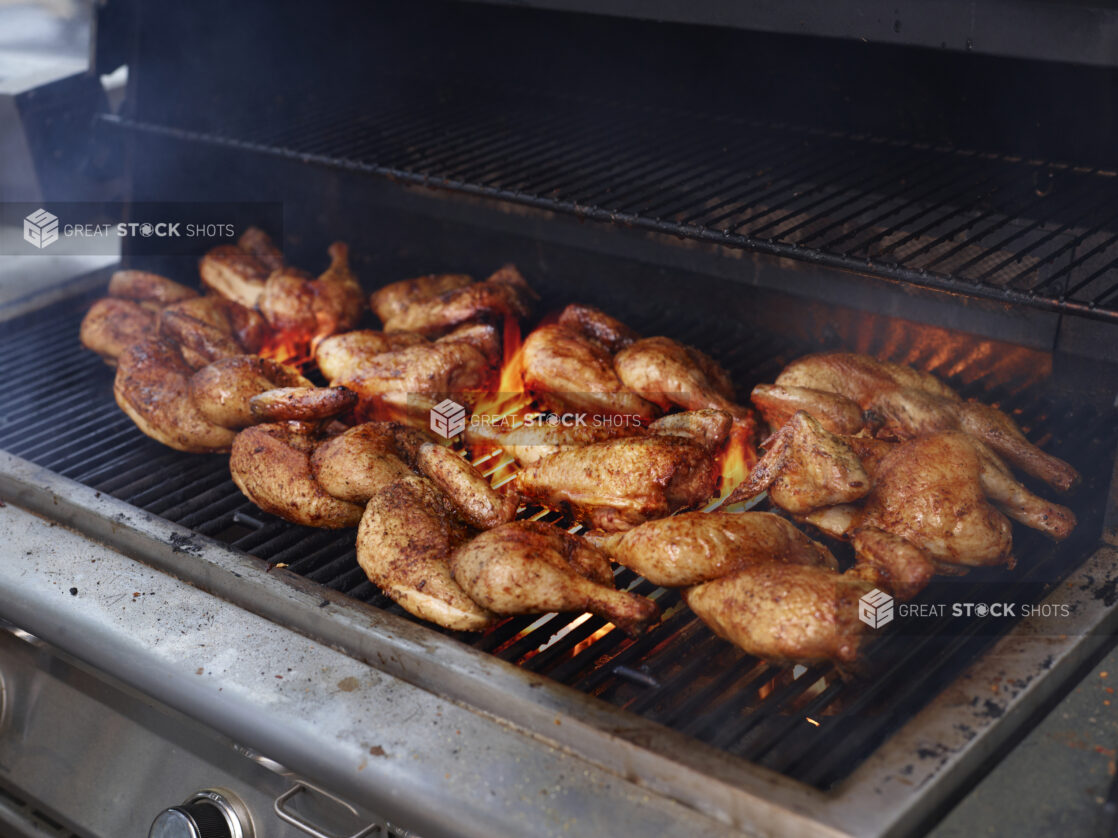 Whole seasoned chickens grilling on a barbecue grill with open flames