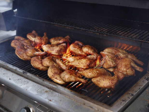 Whole seasoned chickens grilling on a barbecue grill with open flames