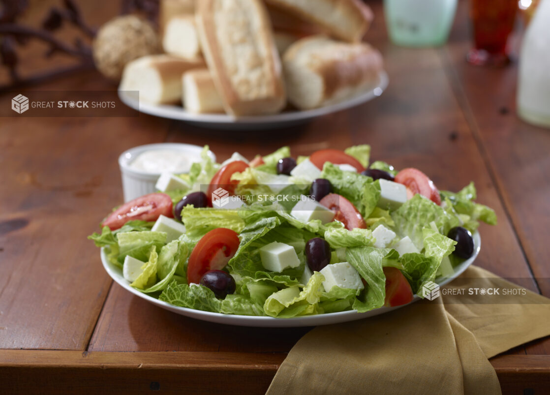 Close Up of a Greek Salad with Romaine Lettuce, Sliced Tomatoes, Olives and Cubed Feta Cheese in a Restaurant Dining Setting