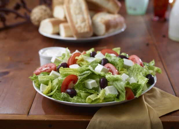 Close Up of a Greek Salad with Romaine Lettuce, Sliced Tomatoes, Olives and Cubed Feta Cheese in a Restaurant Dining Setting