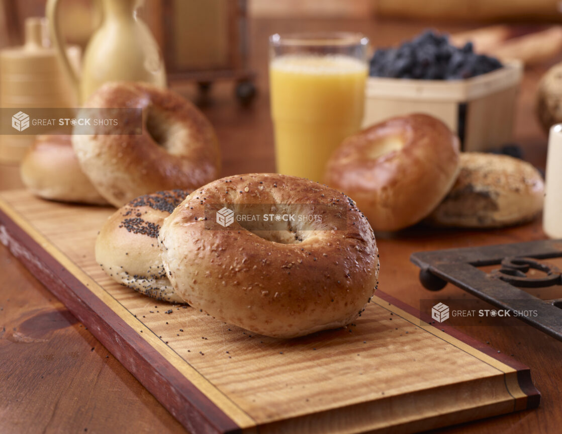 Close Up of Whole Wheat and Poppy Seed Bagels with a Glass of Orange Juice on a Wood Board in an Indoor Kitchen Setting