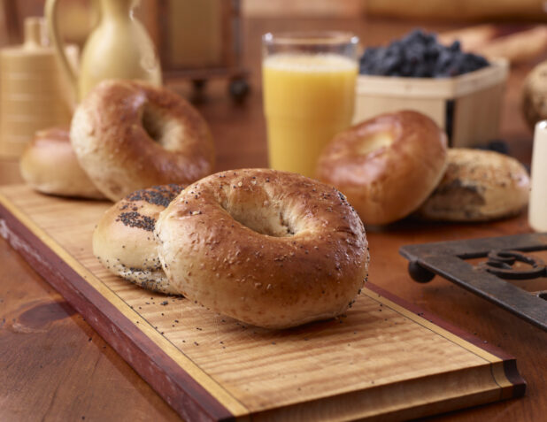 Close Up of Whole Wheat and Poppy Seed Bagels with a Glass of Orange Juice on a Wood Board in an Indoor Kitchen Setting