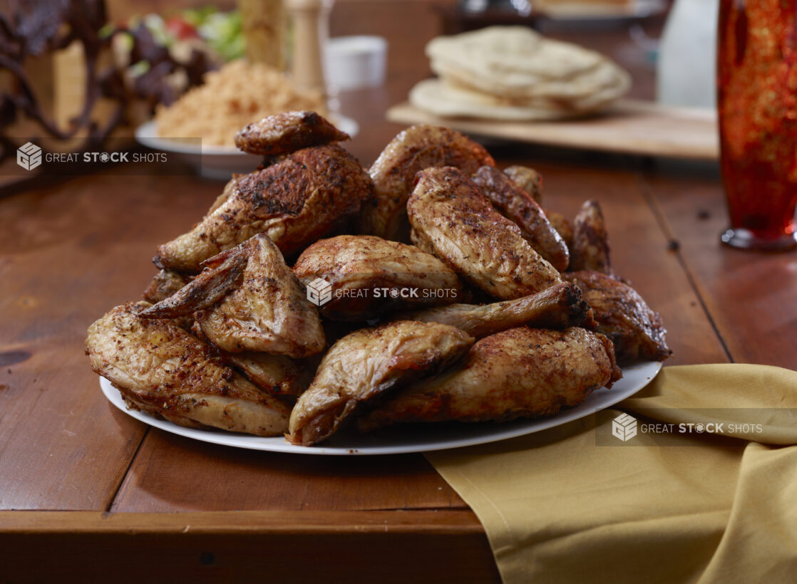 A Platter of Rotisserie Chicken Legs and Side Dishes of Spanish Rice and Naan Bread on a Wooden Table in an Indoor Setting