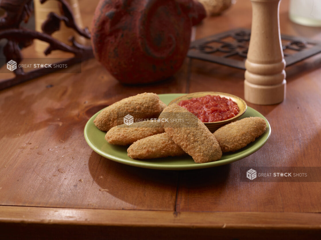 A Plate of Deep Fried Breaded Jalapeño Poppers Served with Marinara Sauce on a Wooden Table Surface in an Indoor Setting