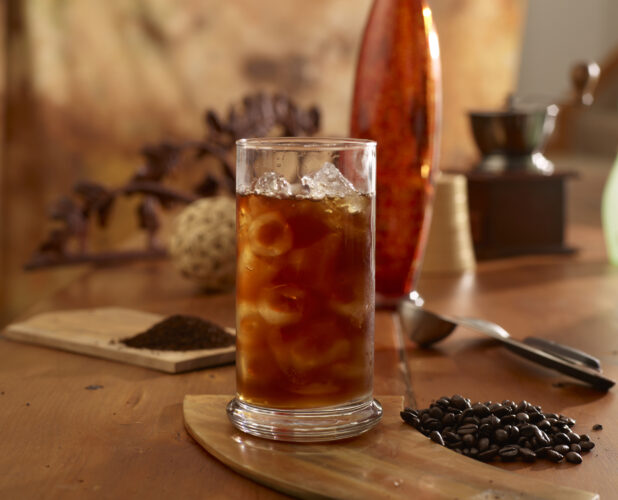 Iced Black Coffee in Glass Cup with Ice Cubes on a Wooden Table with Whole Coffee Beans and Ground Coffee in an Indoor Setting