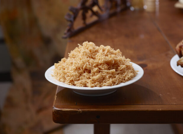 Round White Bowl of Seasoned Mexican Rice on a Wooden Table in an Indoor Setting