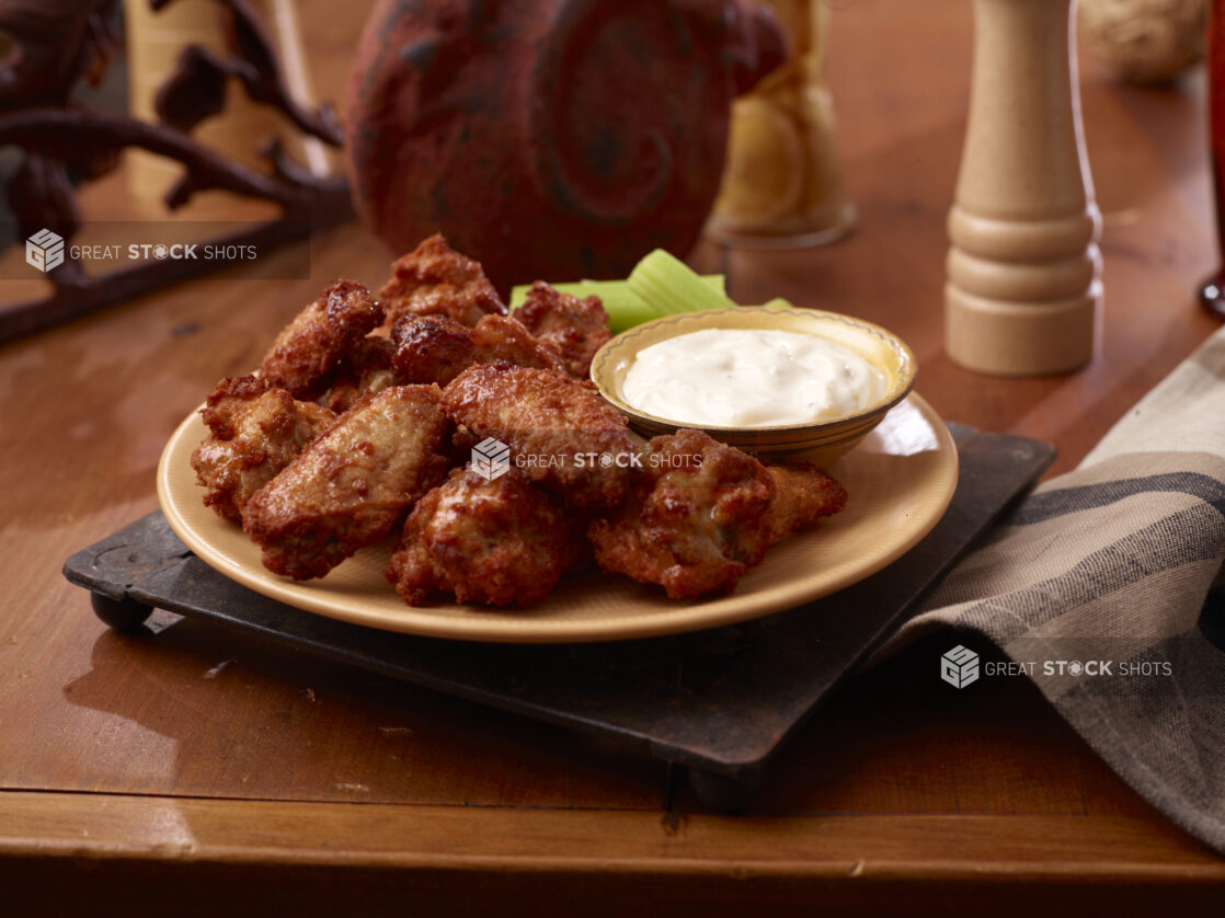 A Plate of Deep Fried Naked Chicken Wings Served with a Side of Ranch Dipping Sauce and Celery Sticks on a Wooden Table Surface in an Indoor Setting