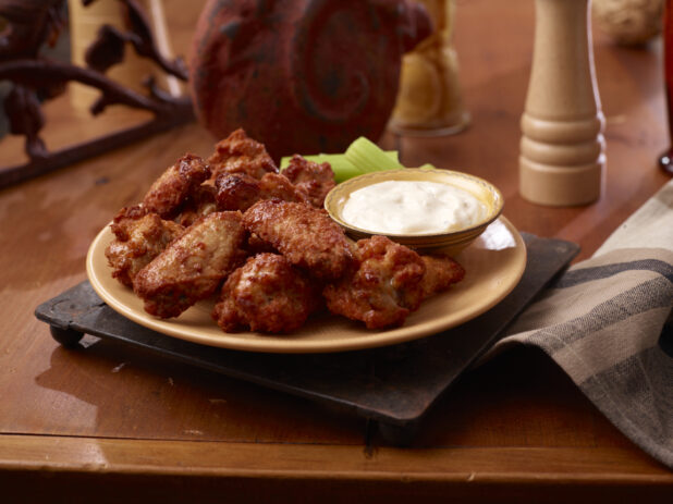A Plate of Deep Fried Naked Chicken Wings Served with a Side of Ranch Dipping Sauce and Celery Sticks on a Wooden Table Surface in an Indoor Setting