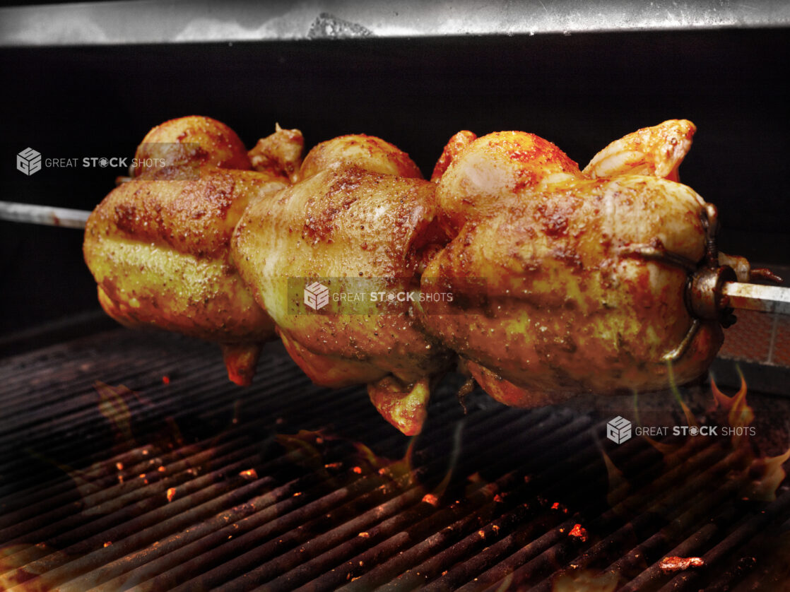 Three Whole Rotisserie Chickens on a Spit Over an Open Flame Barbecue Grill