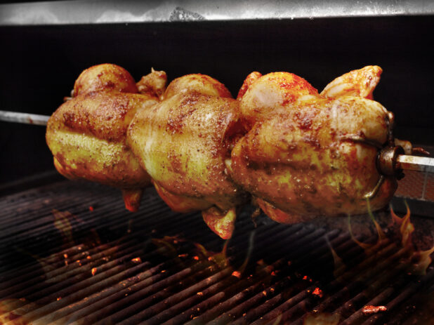 Three Whole Rotisserie Chickens on a Spit Over an Open Flame Barbecue Grill