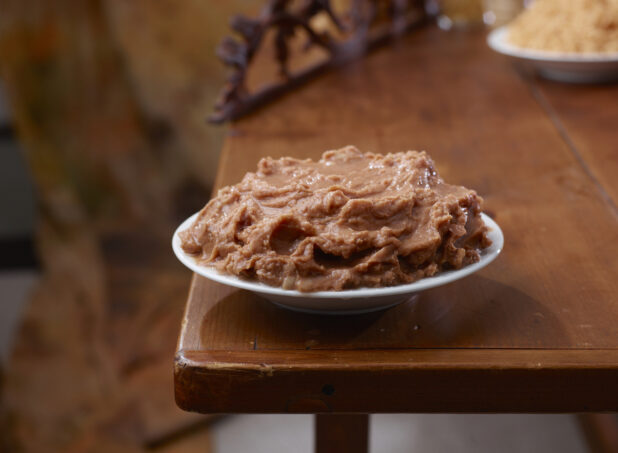 Round White Bowl of Mushy Refried Beans on a Wooden Table in an Indoor Setting