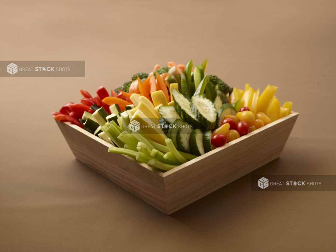 Assorted Fresh Vegetable Sticks in a Deep Wooden Tray on a Brown Background