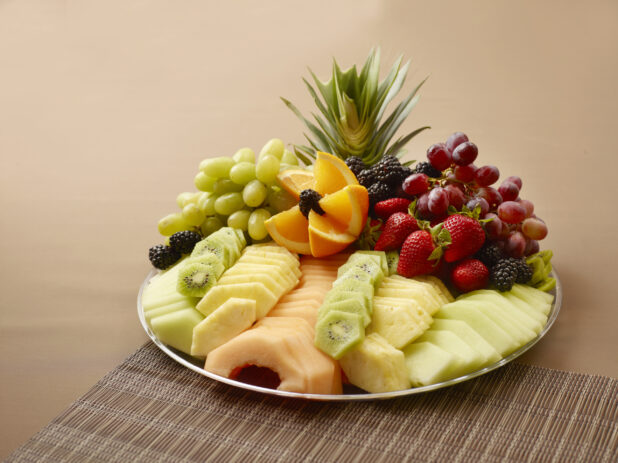 Fresh Fruits Sliced and Whole on a Silver Party Platter on a Brown Background