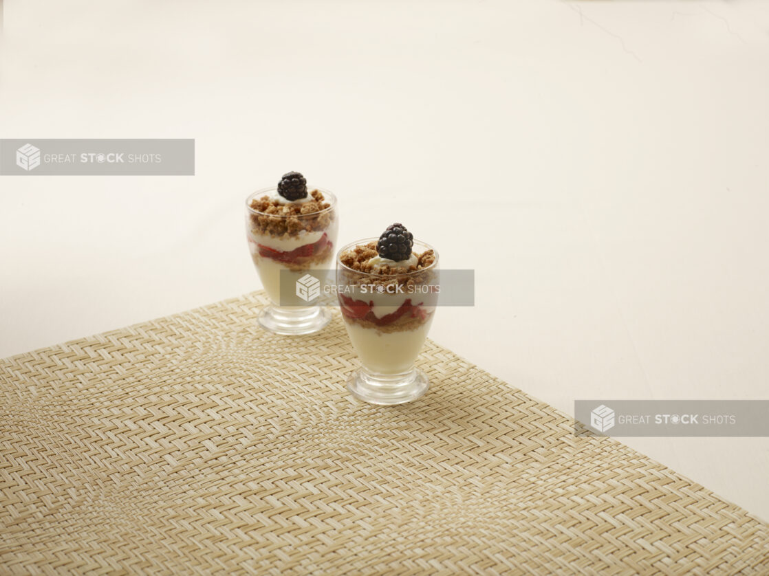 Mini Yogurt Parfait Cups with Fresh Berries and Granola in Miniature Glass Cups on a Beige Background and Placemat - for Catering