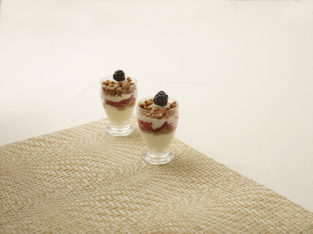 Mini Yogurt Parfait Cups with Fresh Berries and Granola in Miniature Glass Cups on a Beige Background and Placemat - for Catering