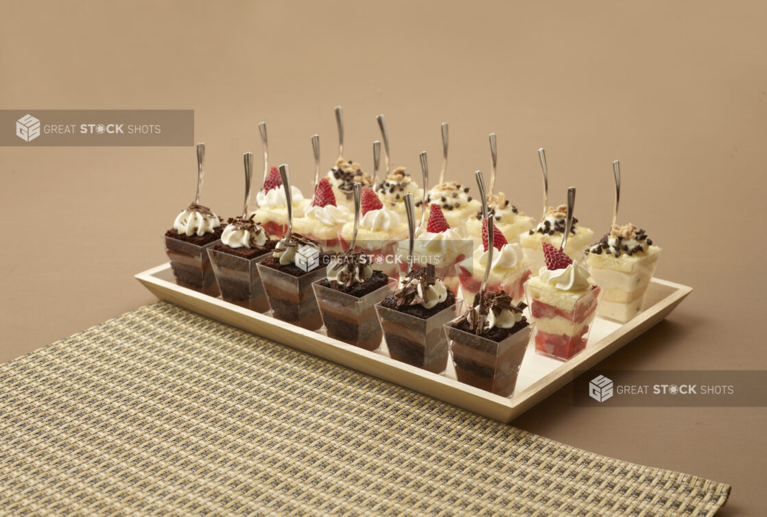 Rectangular Wood Tray with Assorted Mini Dessert Cups - Chocolate Cake, Strawberry Shortcake and Chocolate Chip Cake on a Brown Surface and Placemat - For Catering