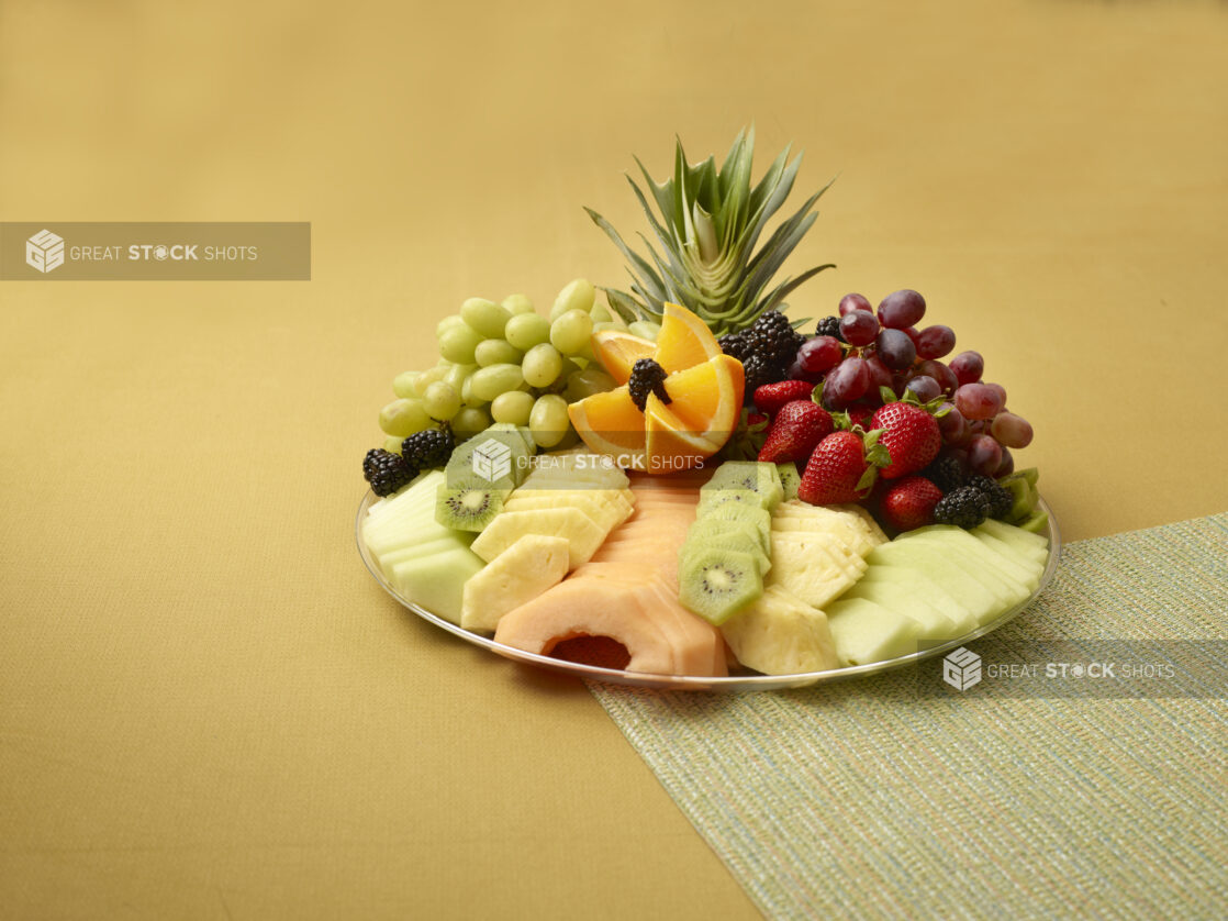 Fresh Fruits Sliced and Whole on a Silver Party Platter on a Yellow Background