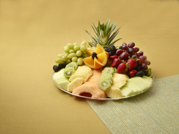 Fresh Fruits Sliced and Whole on a Silver Party Platter on a Yellow Background