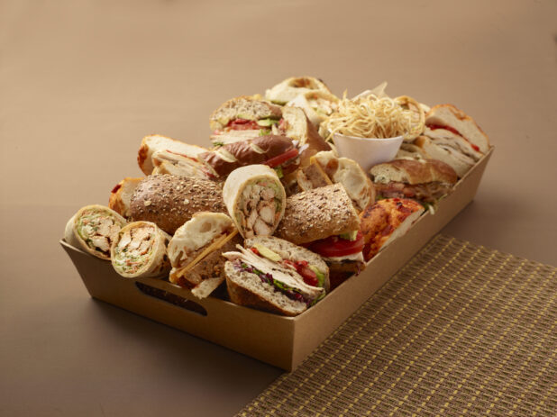Assorted Cold Cut Sandwiches and Wraps in a Wooden Basket Tray for Catering on a Brown Background