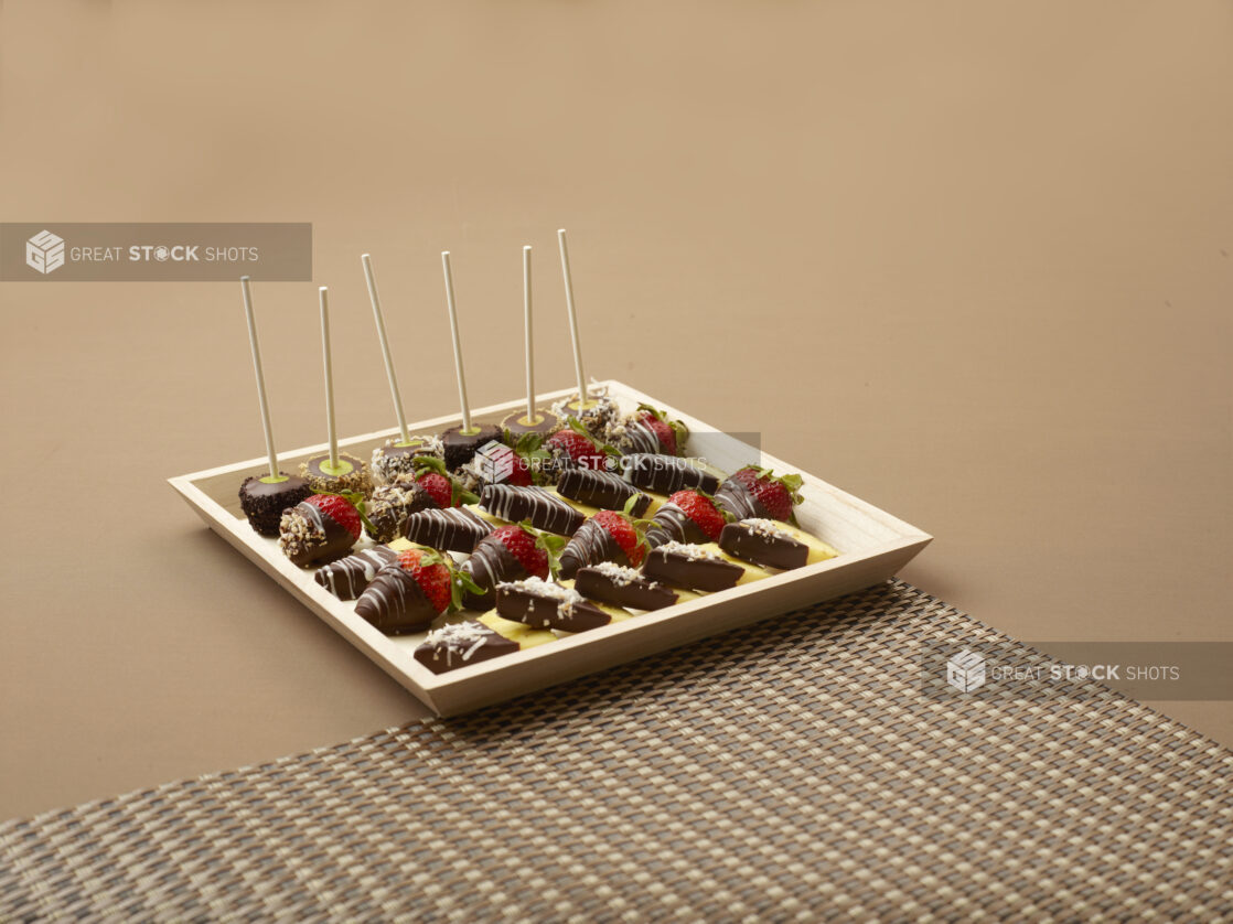 Square Wood Tray with Chocolate Covered Strawberries, Pineapple Wedges and Cake Pops on a Brown Surface and Placemat - for Catering