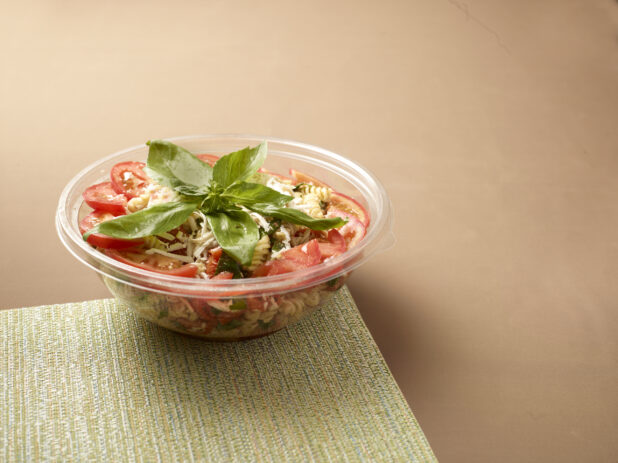 Take-out Container of Pasta Salad with Sliced Tomatoes and Fresh Basil Leaves on a Placemat - Variation