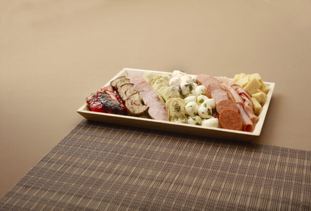 A Rectangular Wood Tray of Antipasto with Assorted Cheese, Deli Meats and Vegetables on a Brown Surface and Placemat