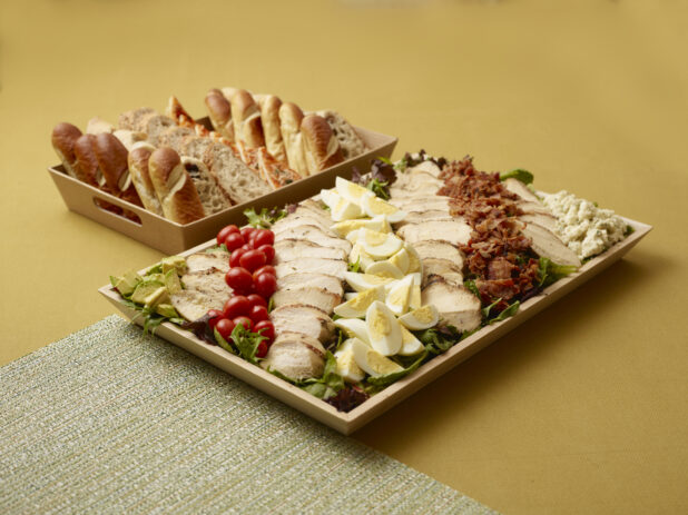 Lunch Catering Package with Large Cobb Salad Platter and Basket of Assorted Breads on a Yellow Background