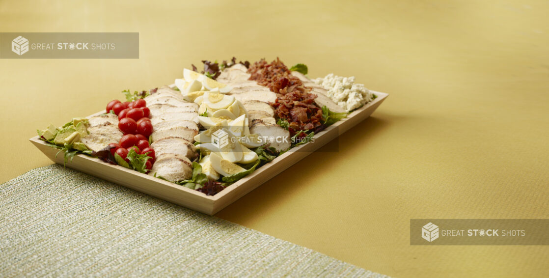 Cobb Salad Platter with Grilled Chicken Breasts on Wooden Serving Tray on Mustard Yellow background