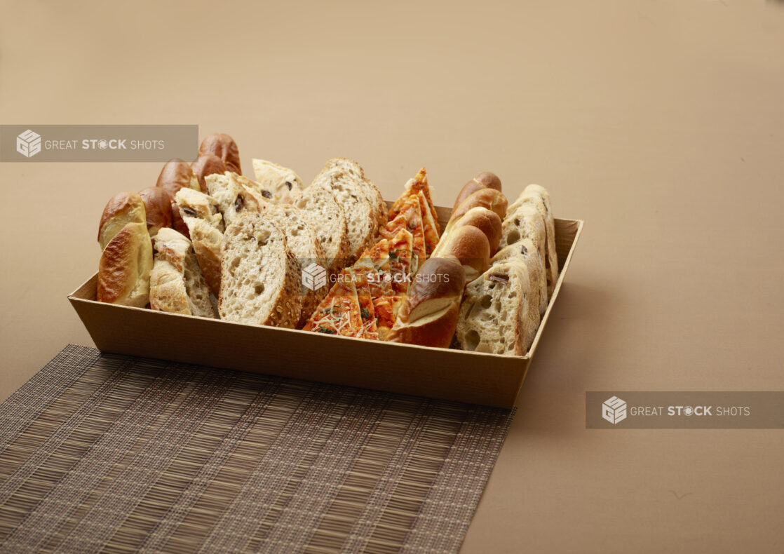 Close Up of a Catering Platter with Assorted Sliced Breads, Flatbreads and Focaccia on a Brown Surface and Placemat