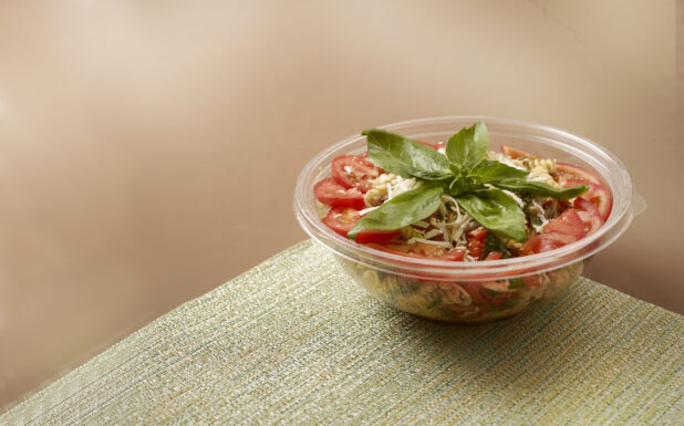 Take-out Container of Pasta Salad with Sliced Tomatoes and Fresh Basil Leaves on a Placemat
