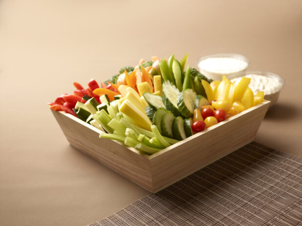 Assorted Fresh Vegetable Sticks in a Deep Wooden Tray on a Brown Background with Placemat and Creamy Dipping Sauces