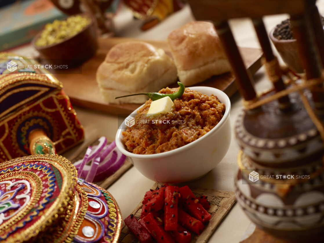 Pav Bhaji - Indian Street Food of a Tomato, Vegetable and Mashed Potato Gravy with Soft Indian Rolls on a Wooden Table in an Indoor Setting