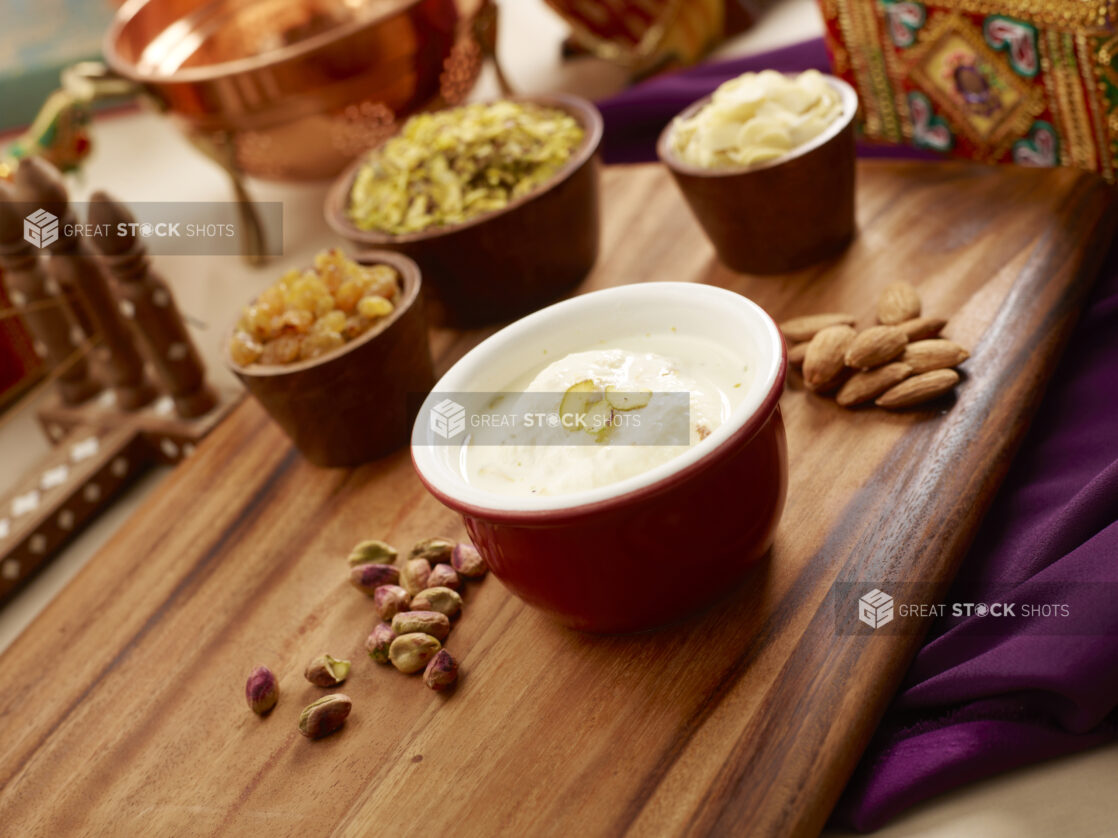 Bowl of Ras Malai - Indian Dessert of Dough Balls Soaked in Malai Clotted Cream with Nuts and Dried Fruits on a Wooden Platter