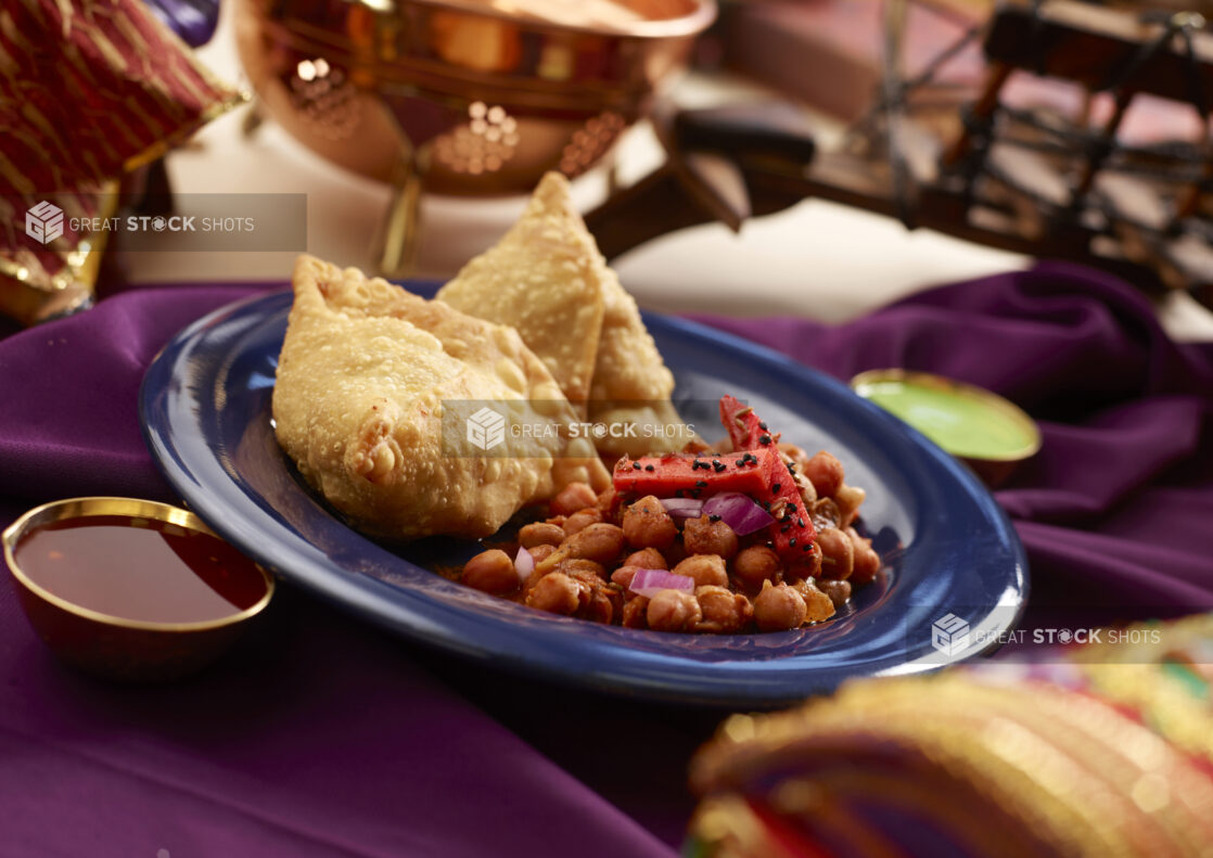 Indian Savoury Snack – Samosas – with Channa Masala Curry on a Blue Ceramic Plate on a Purple Tablecloth in an Indoor Setting