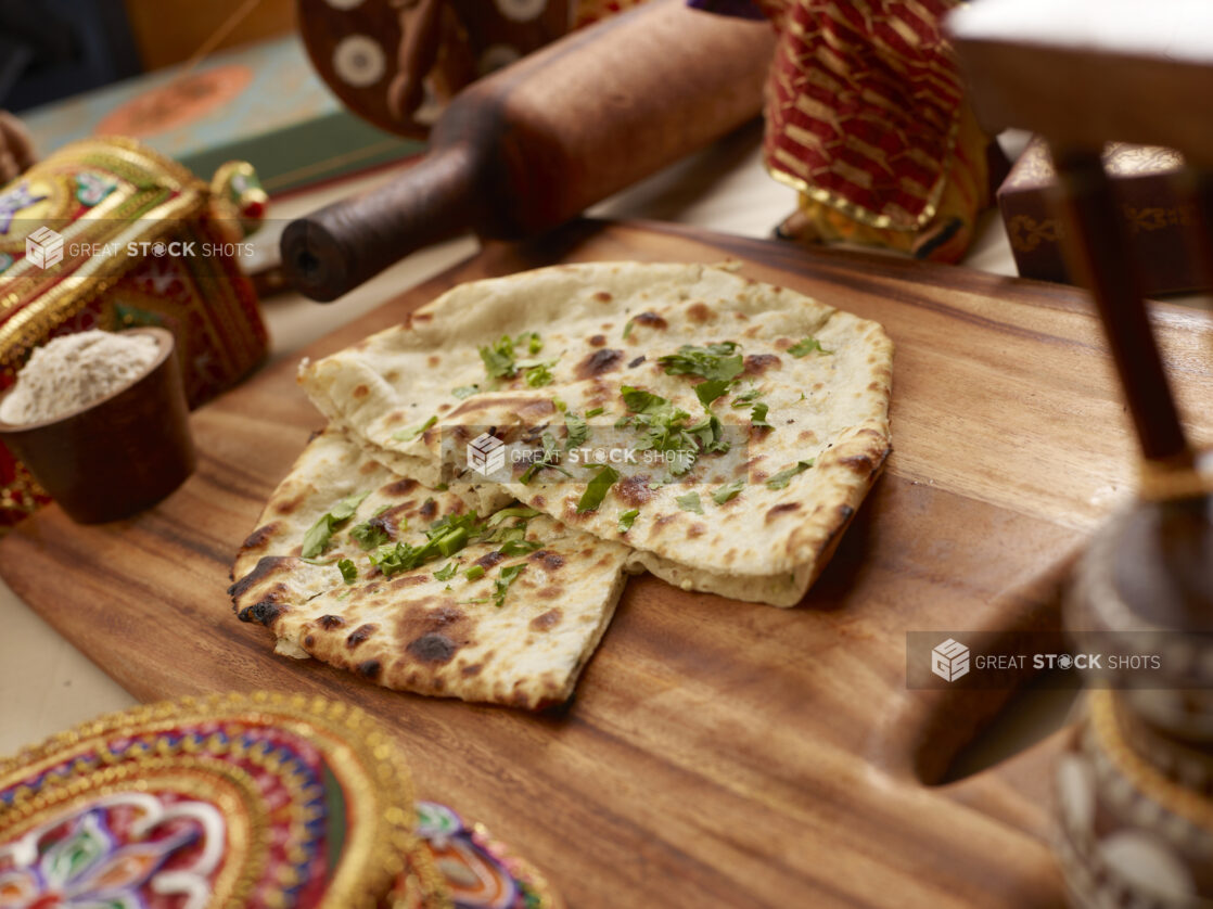 Oven-baked (Tandoor) Plain Naan – Indian Bread - with Chopped Coriander Leaves on a Wooden Cutting Board in an Indoor Setting