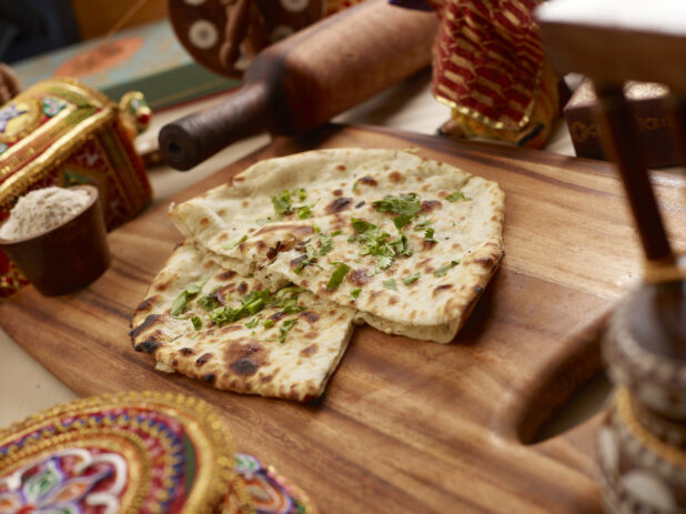 Oven-baked (Tandoor) Plain Naan – Indian Bread - with Chopped Coriander Leaves on a Wooden Cutting Board in an Indoor Setting