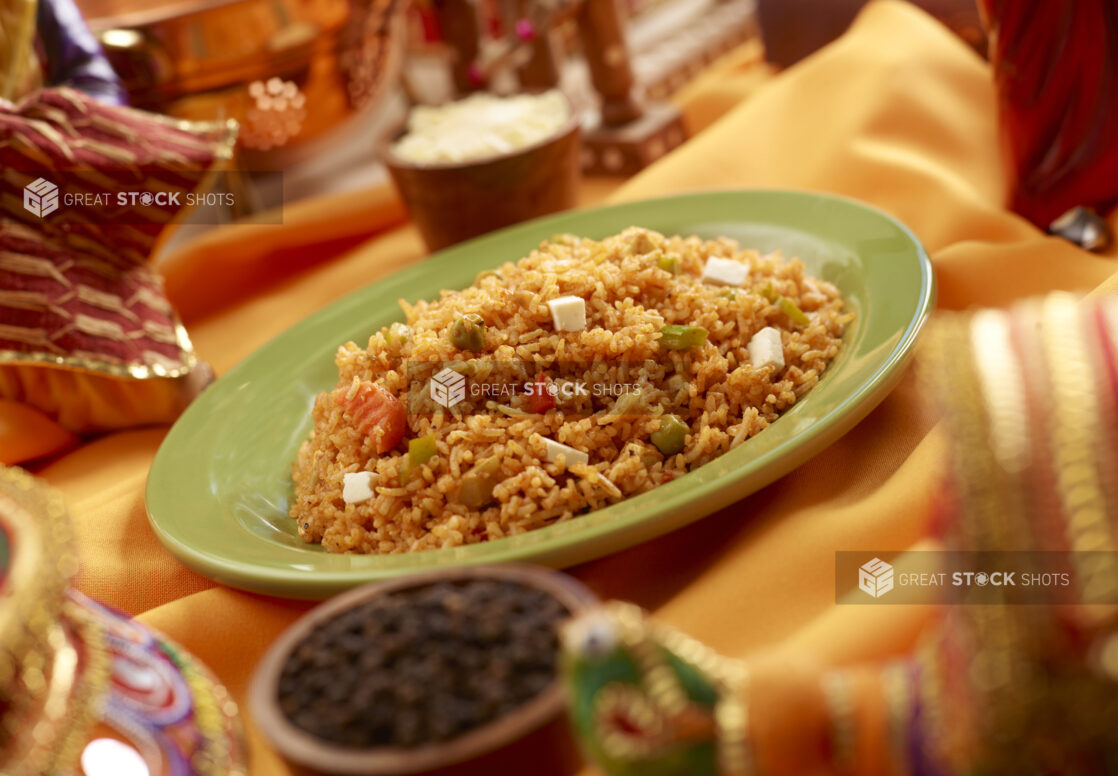 Vegetable and Paneer Pulao Indian Rice Dish in a Green Ceramic Bowl on a Orange Table Cloth in an Indoor Setting