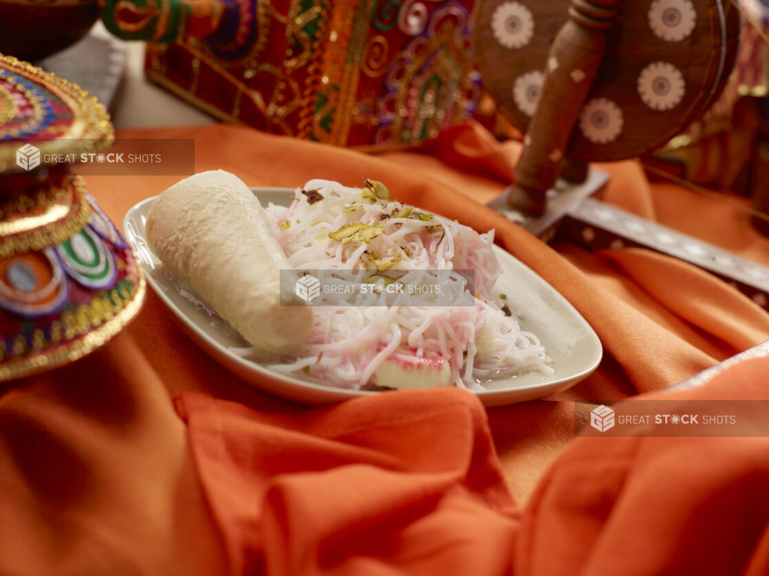 Indian Dessert Dish of Sweet Rice Vermicelli Noodles, Milk Pudding and Crushed Pistachios on a Rounded Square Ceramic Plate on an Orange Tablecloth