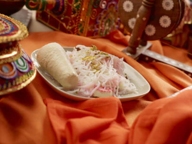 Indian Dessert Dish of Sweet Rice Vermicelli Noodles, Milk Pudding and Crushed Pistachios on a Rounded Square Ceramic Plate on an Orange Tablecloth