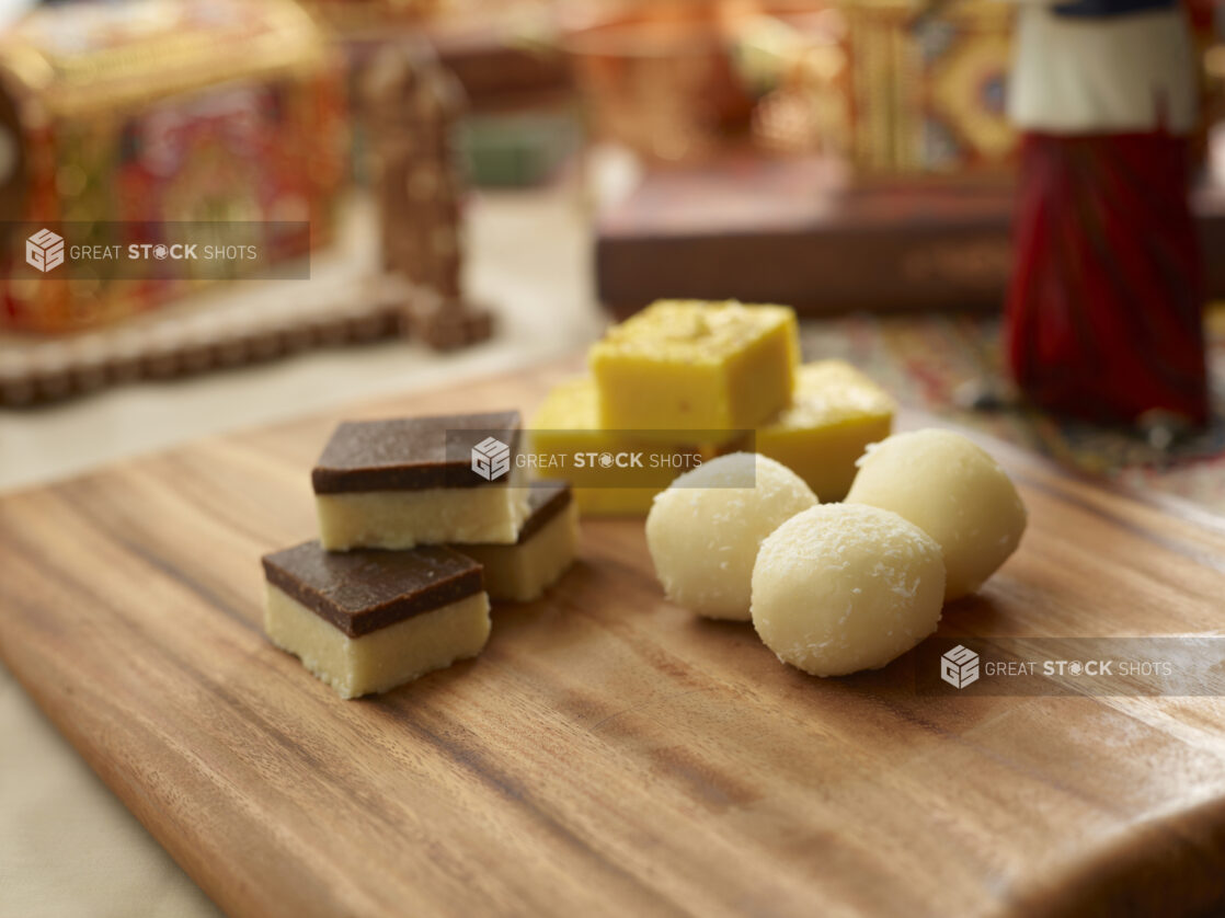 Assorted Sweet Indian Dessert Squares and Balls on a Wooden Platter in an Indoor Setting