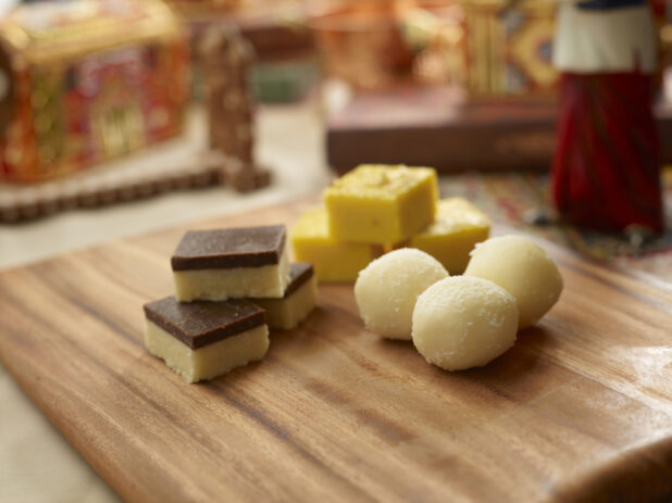 Assorted Sweet Indian Dessert Squares and Balls on a Wooden Platter in an Indoor Setting