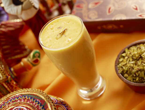 Tall Glass of Mango Lassi - an Indian Yogurt-Based Beverage - on an Orange Tablecloth in an Indoor Setting