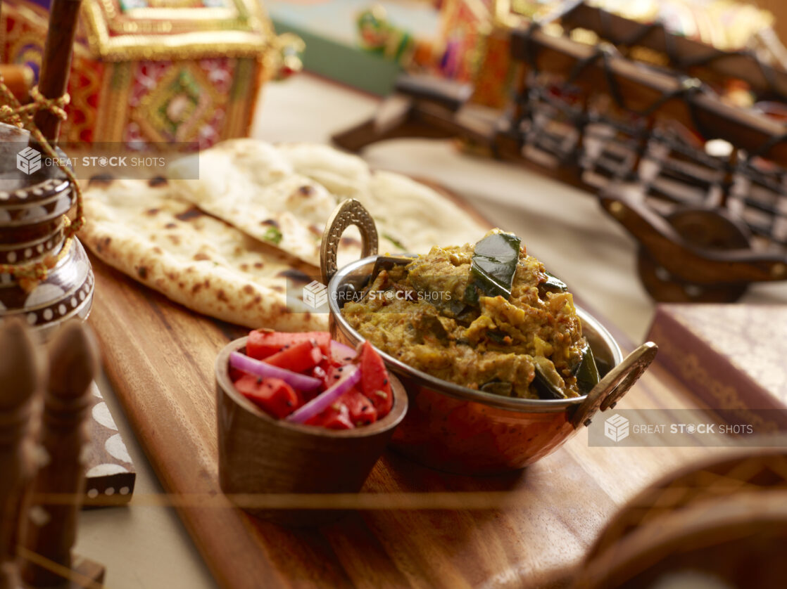 Copper Bowl of Vegetable Poha on a Wooden Platter with Fresh Naan Bread and a Bowl of Pickled Vegetables in an Indoor Setting